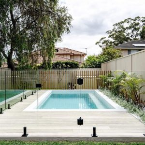 Rectangular in-ground backyard pool with blue water and beige tiled flooring.