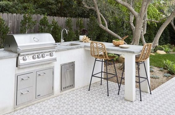 Outdoor kitchen with built-in BBQ gas cooker, sink & bench with two bar chairs for alfresco dining.