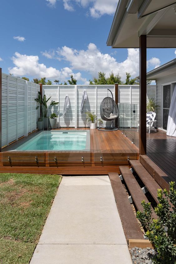Above-ground rectangular pool built into a home deck with corner chair and surrounding plants.