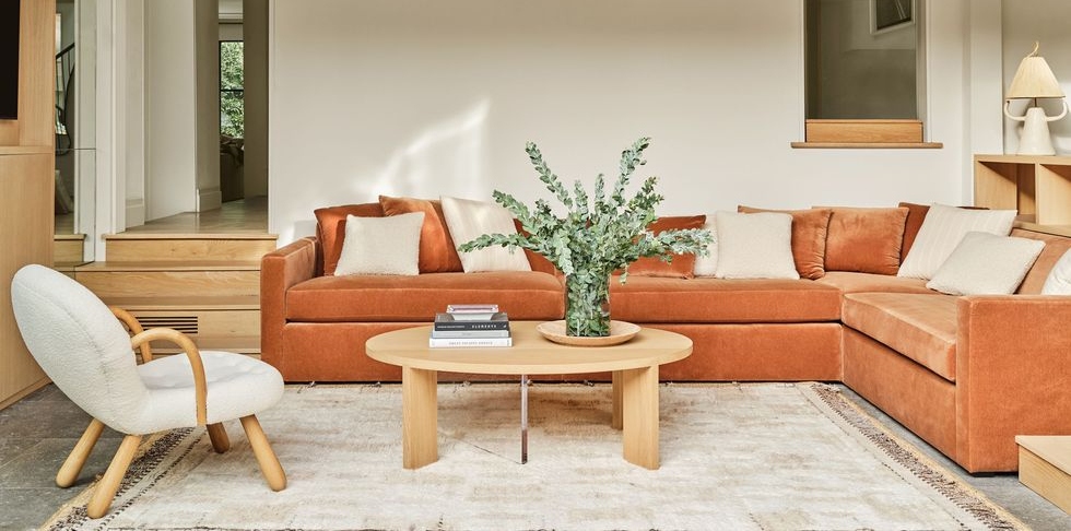 Pastel living room home décor with orange sofa, beige chair, rug, coffee table and plants.