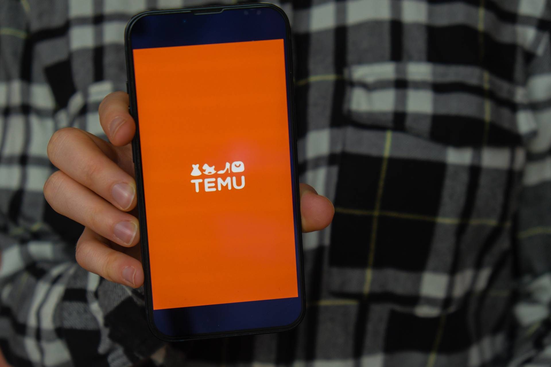a person holding a smartphone displaying the orange temu app screen