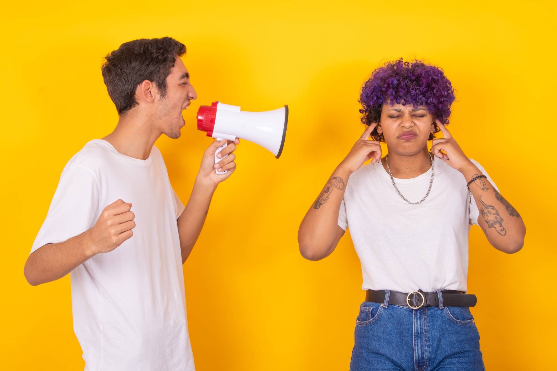 a person yelling into a megaphone while another covers their ears